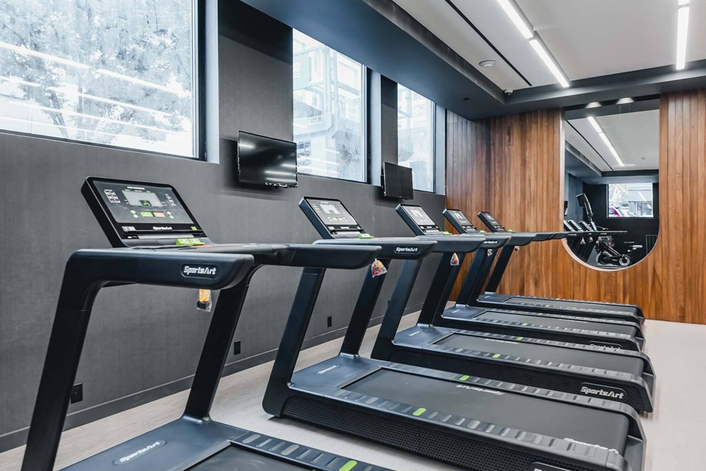 a row of treadmills in a gym with a large window